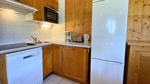 Una cocina compacta con armarios de madera, un refrigerador blanco, un microondas, un tostador y una cafetera.