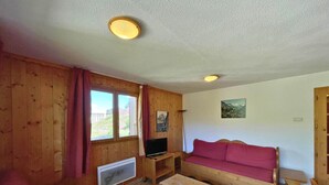 Habitación con paneles de madera, un sofá rojo, una mesa de madera, un televisor y una ventana con cortinas.