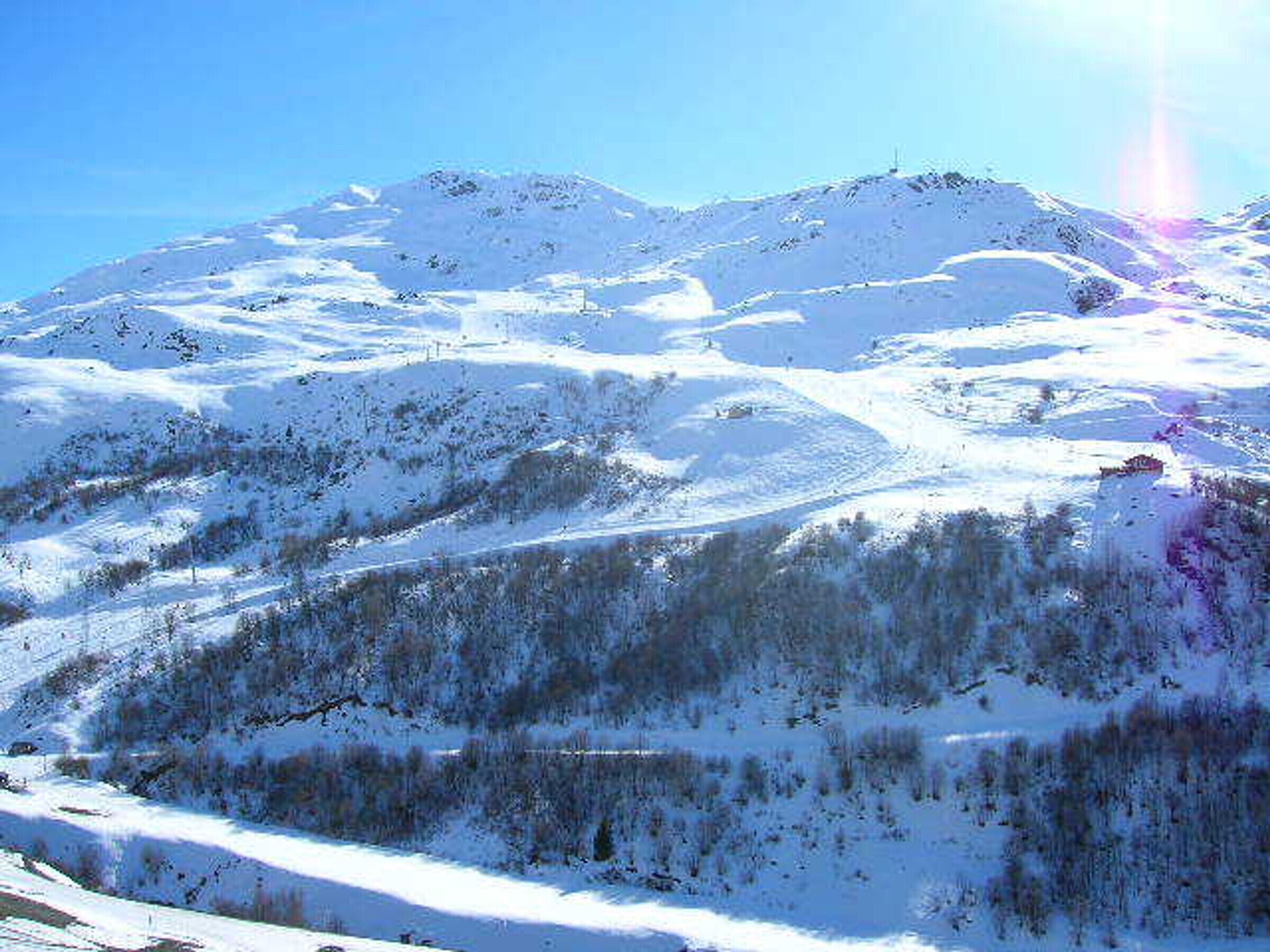 Paesaggio montano innevato con cielo sereno e il sole ben visibile.