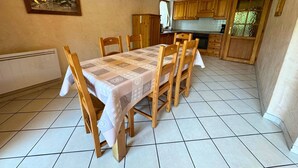 A dining area with a table set for four, wooden chairs, a patterned tablecloth, and a painting on the wall.