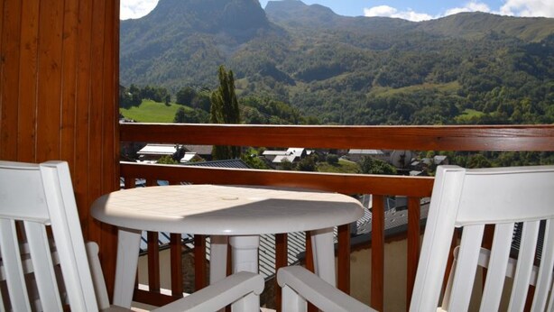A balcony with a table and chairs, overlooking a mountainous landscape.