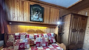 A cozy wooden room with a bed featuring a red and white quilt, a wooden headboard, and a framed picture above the bed. - Ski-in equipped studio - Les Menuires (Les Menuires)