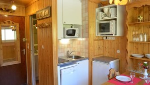 A compact kitchen with wooden walls, a microwave, a small refrigerator, and a dining area with a table set for two. - Ski-in equipped studio - Les Menuires (Les Menuires)
