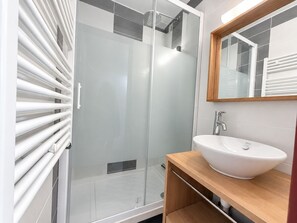A modern bathroom with a glass shower enclosure, a white sink, and a wooden vanity.