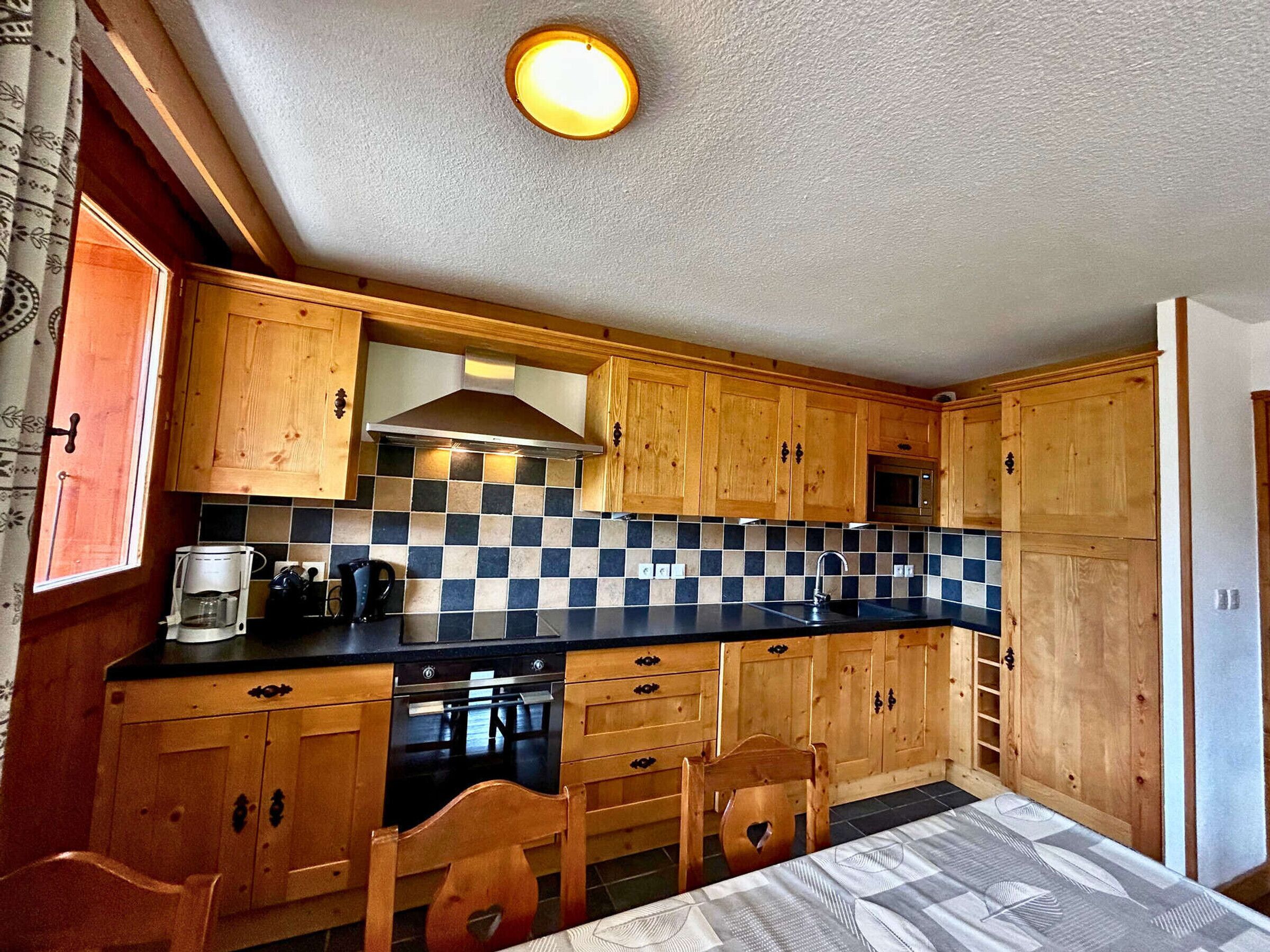 A compact kitchen with wooden cabinets, a checkered backsplash, and a built-in oven.