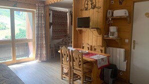 Une pièce chaleureuse avec une table en bois, des chaises, un téléviseur et une machine à café.