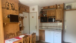Une cuisine compacte avec des meubles en bois, un four à micro-ondes, un évier et un lave-vaisselle. On y trouve une table à manger avec des chaises et un petit tabouret.