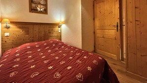 Un dormitorio con cabecera de madera, una cama grande con manta roja, una lámpara de pared y una puerta de madera.