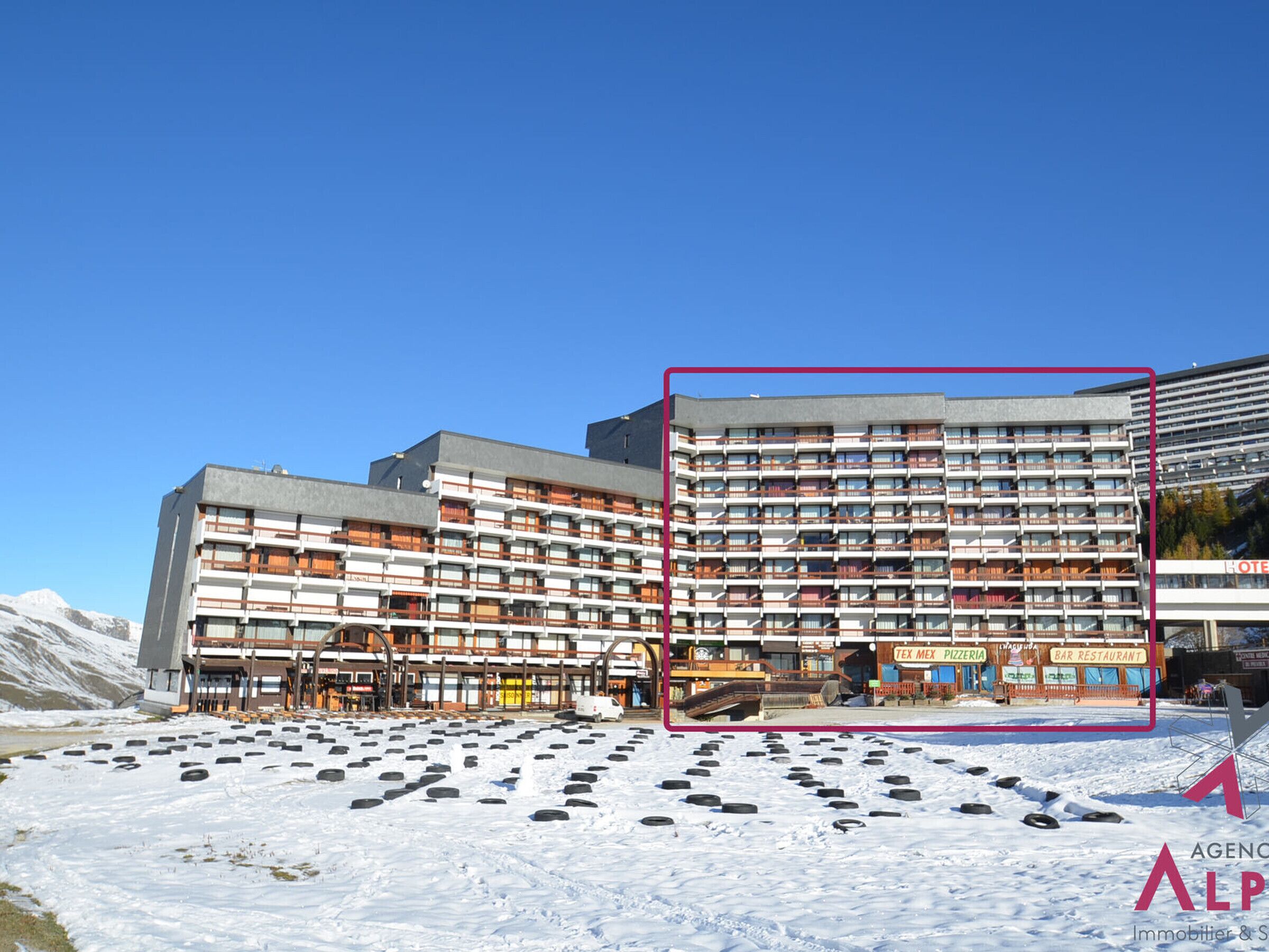 Un hôtel à plusieurs étages, doté d’une architecture moderne, avec des balcons et une piste de ski en premier plan.