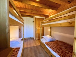 A cabin with two bunk beds, wooden beams, and a wooden door.