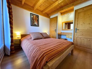 Quarto com estrutura de madeira, cama, mesa de cabeceira, abajur, porta e espelho.