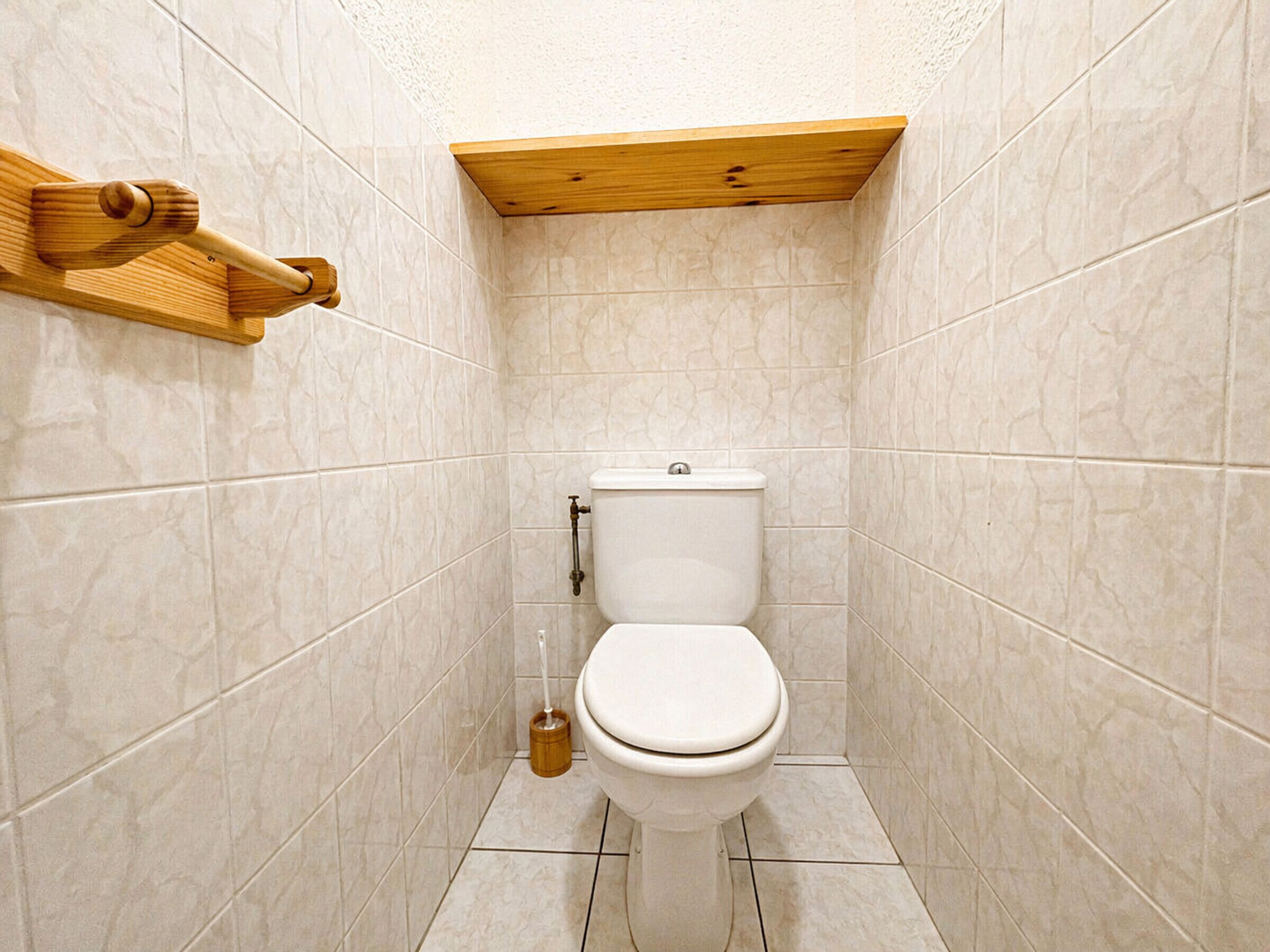 Un baño pequeño con azulejos, un inodoro, un estante de madera y un escobillón.