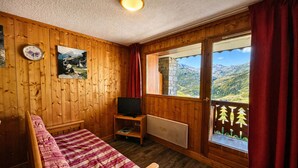 Een houten kamer met een bed, een televisie, een raam met uitzicht op de bergen en een klok aan de muur.