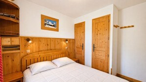 Een slaapkamer met een houten hoofdbord, een bed met wit beddengoed, een houten garderobe, een houten deur en een wandlamp.