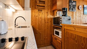Een keuken met houten kastjes, een roestvrijstalen spoelbak, een magnetron en een koffiezetapparaat.