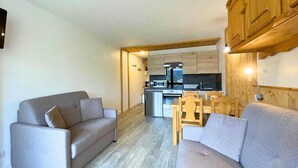 A compact living space with a sofa, a dining table with chairs, a kitchenette, and a wooden ceiling.