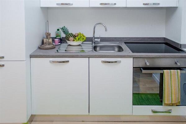 Una cocina con un lavamanos de acero inoxidable, un bol de fruta y una toalla verde colgada en la puerta.