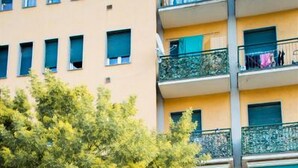 Un edificio de varios pisos con balcones, una entrada protegida por una reja y un árbol en la parte delantera.