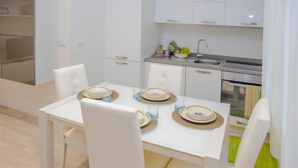 Una cocina moderna con armarios blancos, un lavamanos de acero inoxidable y un comedor con una mesa dispuesta para cuatro.