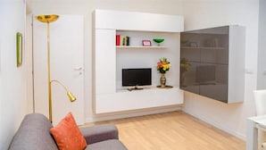 Una sala de estar moderna con un sofá gris, un televisor de pantalla plana y un mueble blanco con estantes.