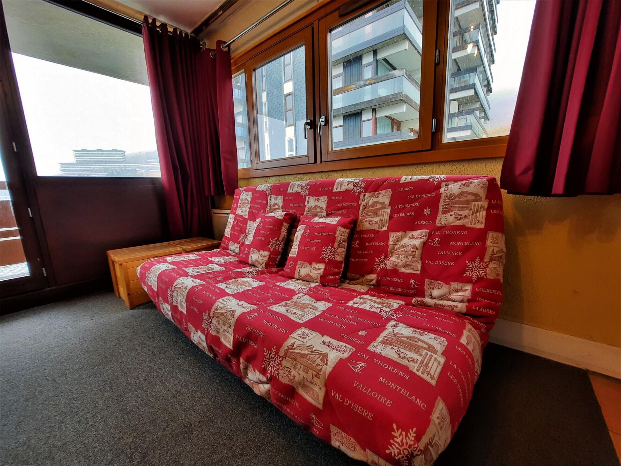 Una habitación con un sofá de estampado rojo y blanco, un banco de madera y una ventana con cortinas rojas.