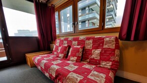 Una habitación con un sofá de estampado rojo y blanco, un banco de madera y una ventana con cortinas rojas.