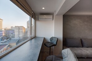 A modern room with a large window, a sofa, a bar stool, and an air conditioning unit.