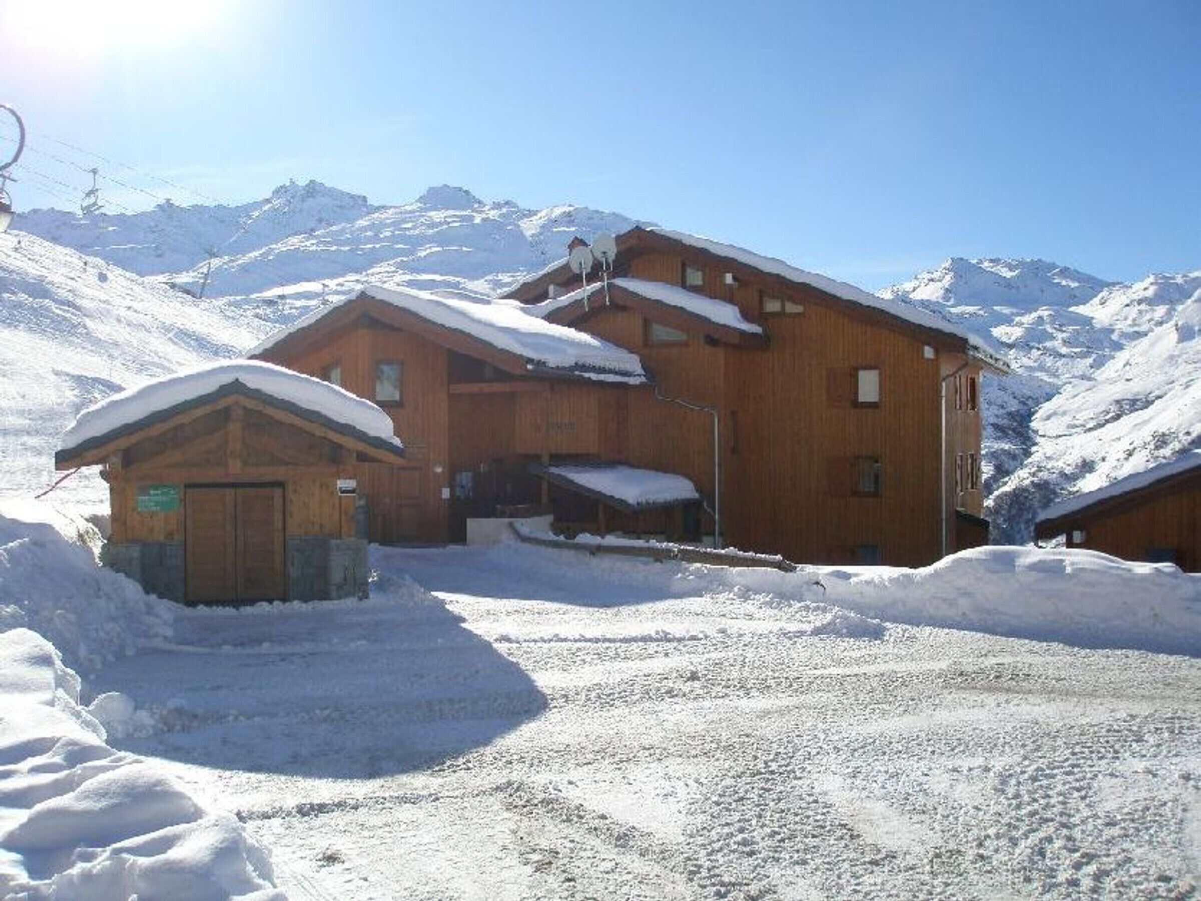 Eine Holzhütte mit verschneitem Dach, vor einer Bergkulisse gelegen.