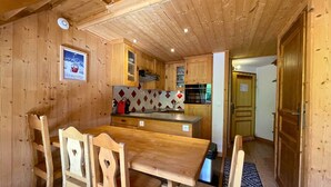 Een houten interieur met een eettafel en stoelen, een keuken met houten kastjes, en een decoratieve spatwand.