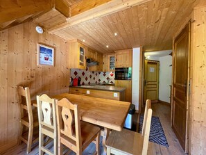 Ein Holzinterieur mit Esstisch und Stühlen, einer Küchenzeile mit Holzausbau und einer gemusterten Spritzschutzwand.