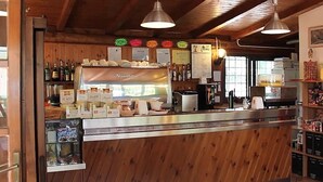 A wooden interior with a counter displaying various food items and a menu board. - Azzurro Camping Village (Bracciano)