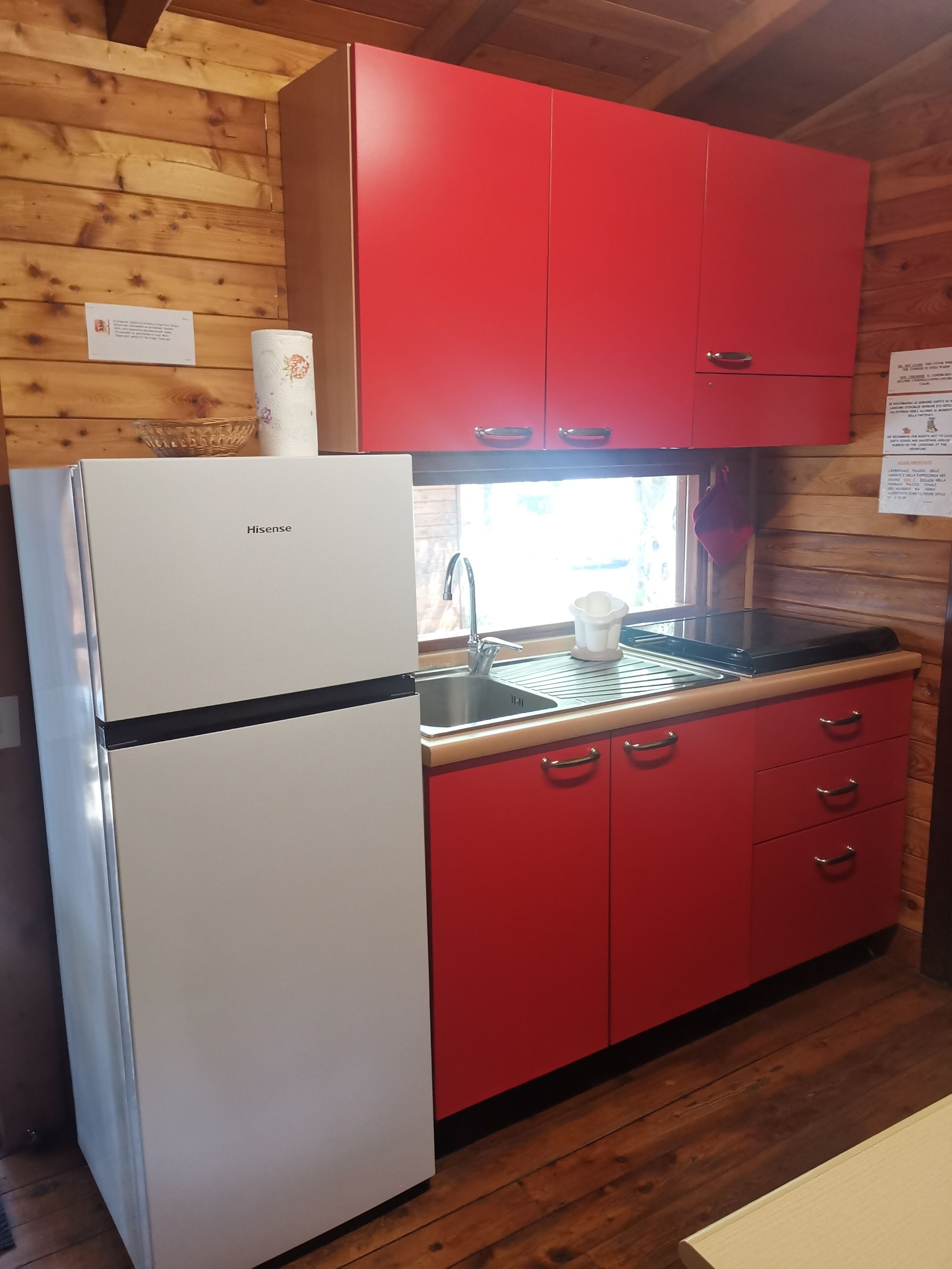 A compact kitchen with a white refrigerator, red cabinets, a sink, and a window with natural light.
