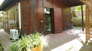 A wooden building with a door and windows, a small air conditioning unit, and a potted plant in the foreground. - Azzurro Camping Village (Bracciano)