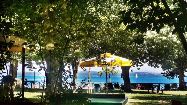 An outdoor seating area with a view of the sea, featuring a table and chairs under a yellow umbrella. - Azzurro Camping Village (Bracciano)