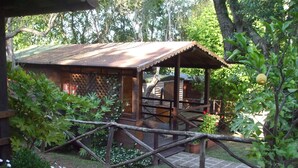 A rustic wooden structure with a metal roof, surrounded by lush greenery and a wooden deck. - Azzurro Camping Village (Bracciano)