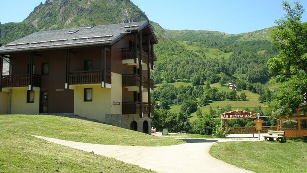 A multi-story building with balconies, a sign for a bar/restaurant, and a mountain in the background.