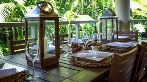 An outdoor dining area with wooden tables, lanterns, and a lush green backdrop.