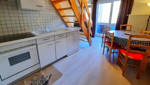 A kitchen with white cabinets, a stove, and a wooden staircase. There is a dining table with chairs and a window with curtains. - Economical apartment with mezzanine for 6 people in Les Menuires (Les Menuires)