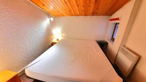 A small, cozy room with a single bed, a nightstand, a lamp, and a window with a view. - Economical apartment with mezzanine for 6 people in Les Menuires (Les Menuires)