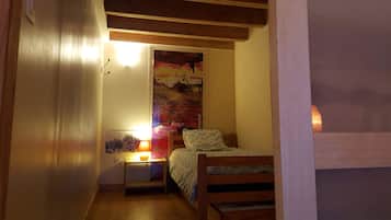 A small bedroom with a bed, a nightstand with a lamp, and a wall-mounted shelf.
