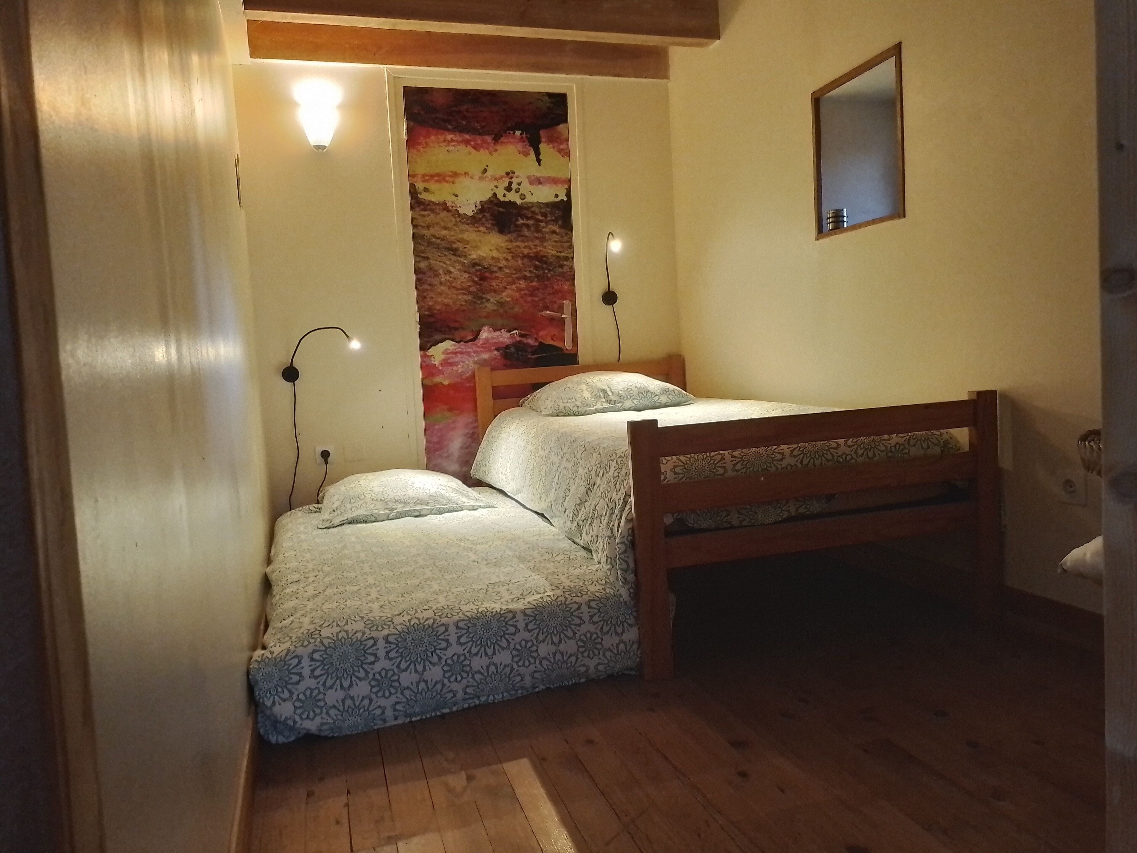 Una habitación pequeña y acogedora con una cama de madera, una mesita de noche y un espejo colgado en la pared.