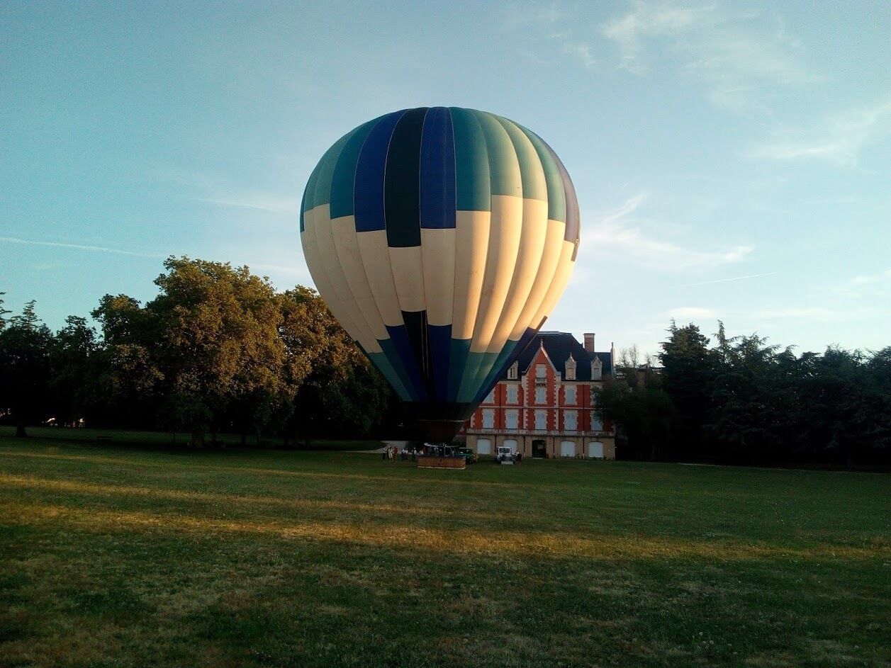Une montgolfière sur un champ herbeux, avec un bâtiment en arrière-plan.
