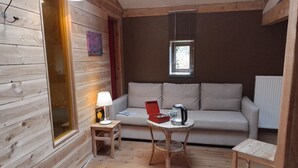 Et hyggeligt værelse med træpaneler, en sofa, et lille bord med elkedel og en lampe.