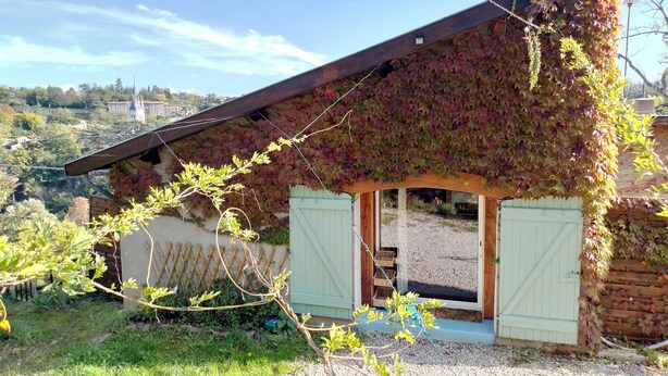 Et rustikt hus med skråt tag, vægge dækket af vedbend og en træveranda.