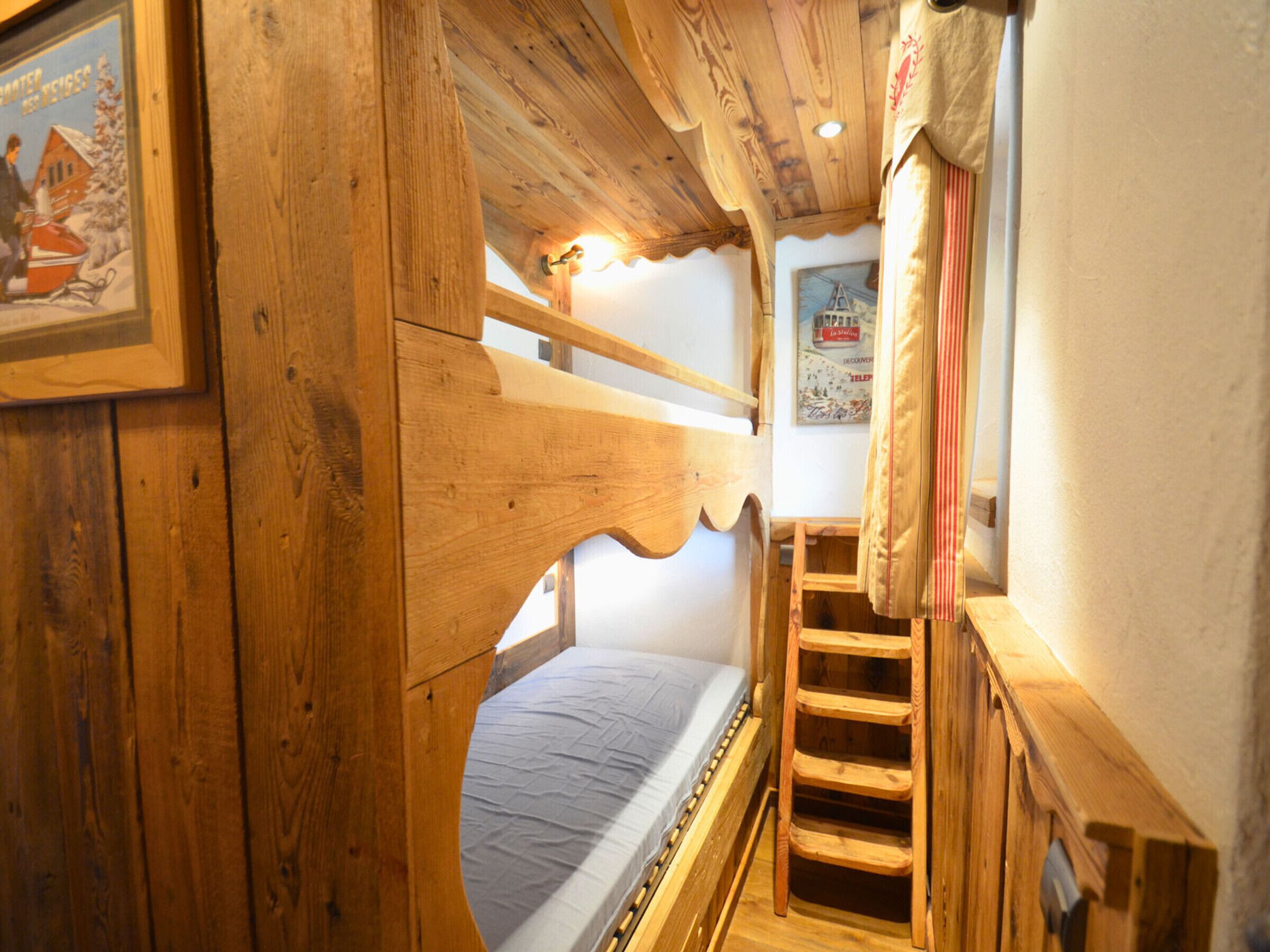 Een houten stapelbed met een ladder, een klein raam en een poster aan de muur.