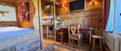 Acogedora habitación tipo cabaña de madera con cama, mesa de comedor y chimenea.