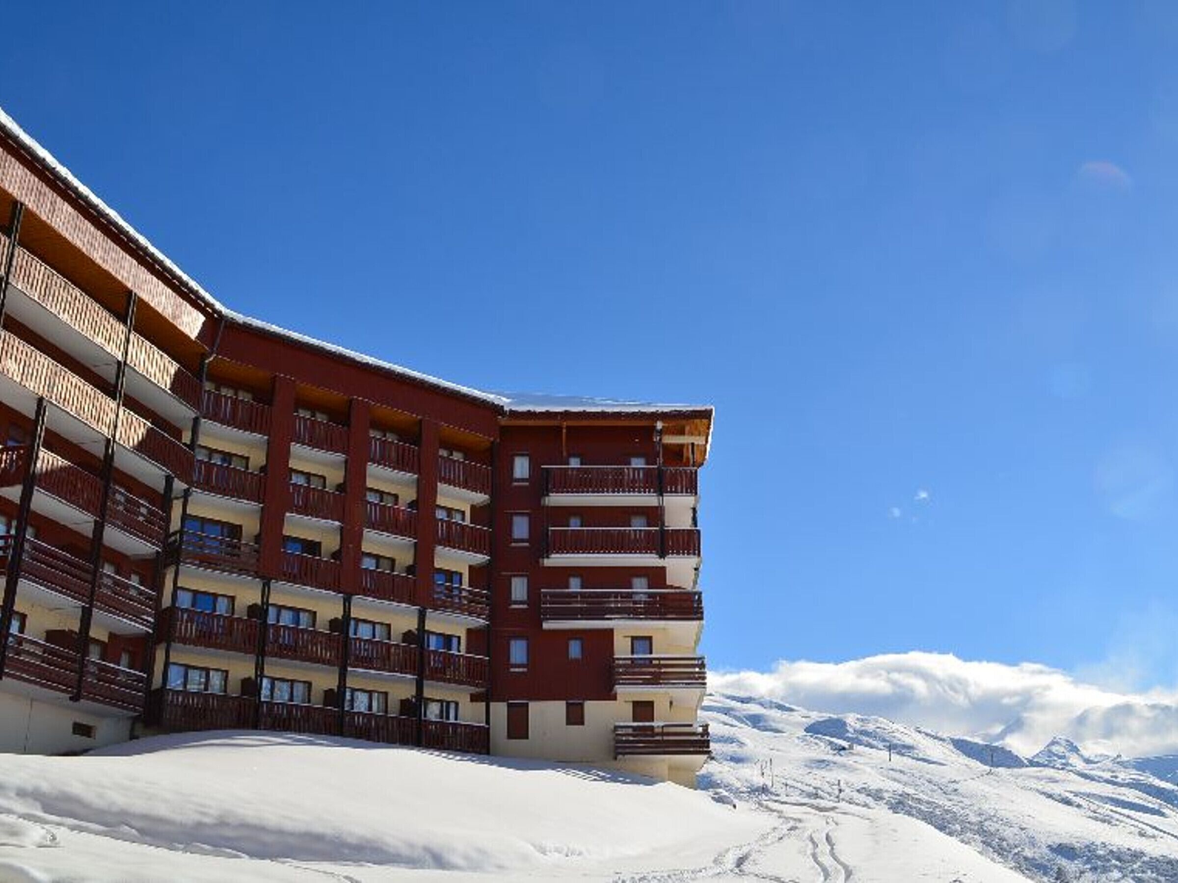 Un hôtel à plusieurs étages, doté de balcons, qui se dresse sur fond de montagnes enneigées.