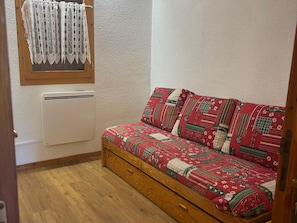 A small room with a wooden floor, a white radiator, a patterned sofa, and a lace curtain.