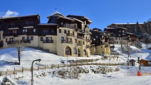 A snow-covered ski resort with multi-story buildings featuring balconies and ski lifts.