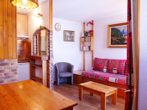 Una sala de estar acogedora con una mesa de comedor de madera, un sofá con una manta estampada, una estantería y un cuadro en la pared.